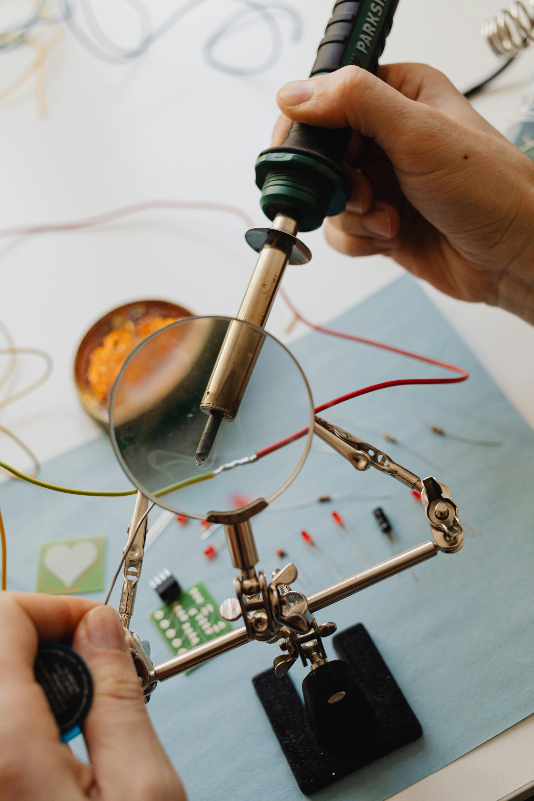 Detailed view of hands soldering electronic components with a magnifying glass and iron.